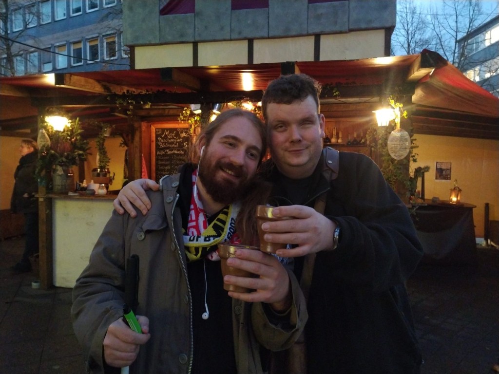 Mit einem Becher heißen, mit stehen mein Kollege und ich auf dem Weihnachtsmarkt