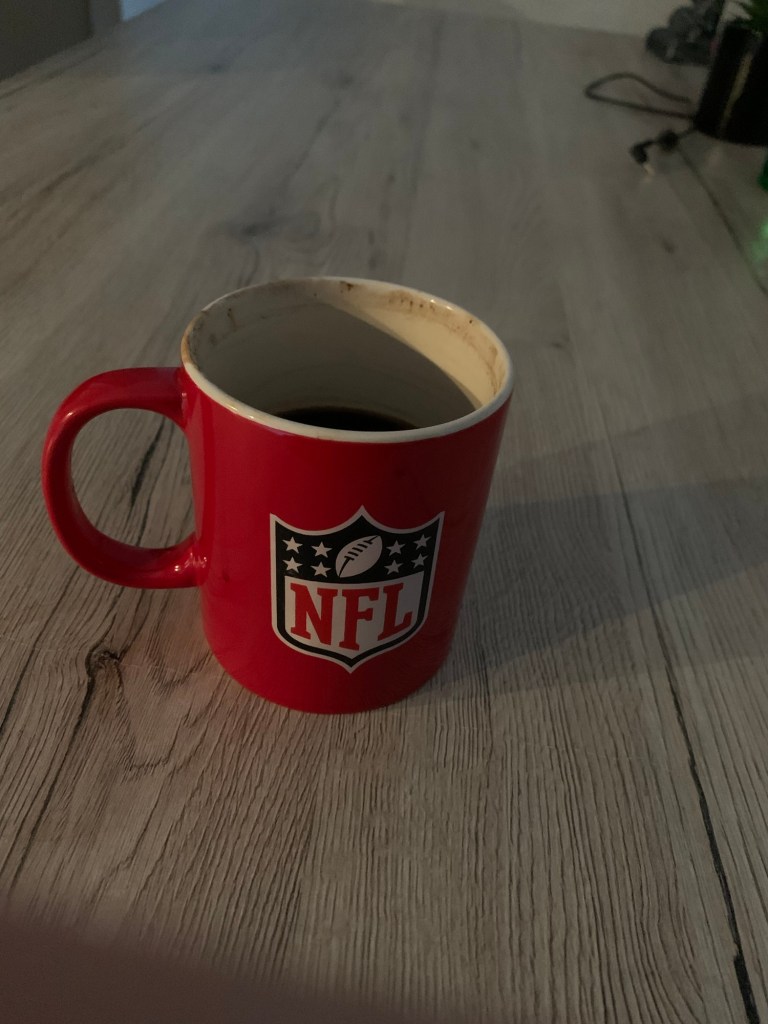 Eine Tasse Kaffee auf einem Holztisch die Tasse ist rot und da drauf ist das NFL Logo zu sehen
